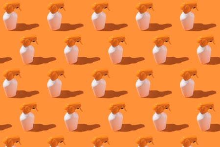 Pattern of white and orange bottles of sunscreen cream with spray on an orange background.